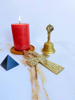 Velón rojo encendido, cruz Ankh dorada, campana tibetana y pirámide de obsidiana para limpieza energética de hogar, oficina y auto.
